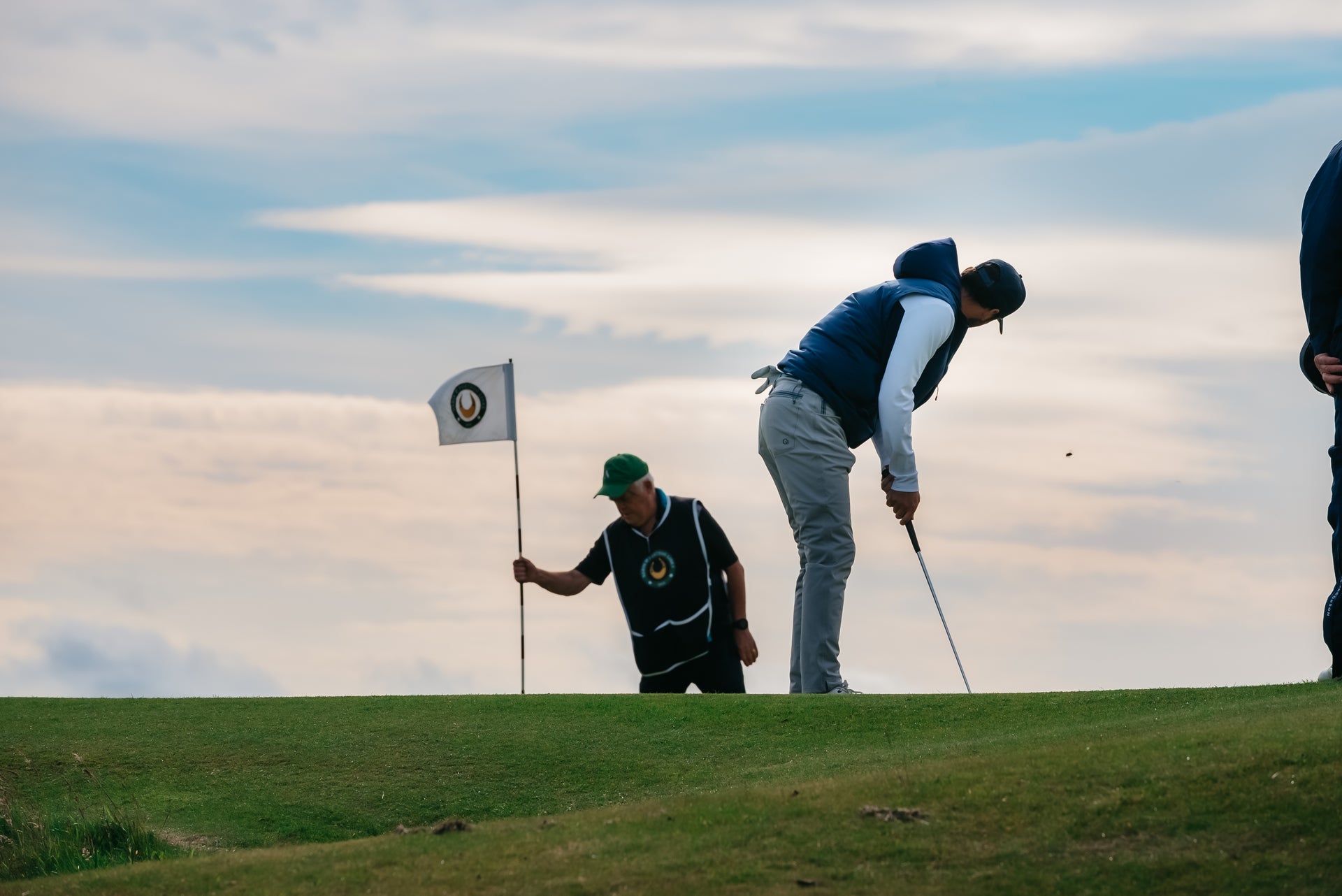 Golfer putting on coastal links course with caddie